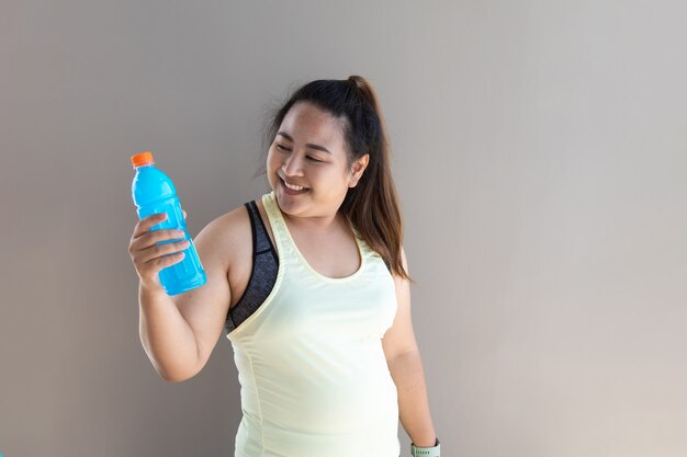 Porträt der übergewichtigen asiatischen Frau in der Sportkleidung, die Flasche Wasser hält