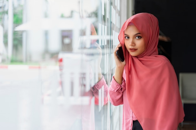 Porträt der überzeugten jungen moslemischen Geschäftsfrau, die rosa hijab am Mitarbeiterraum trägt.