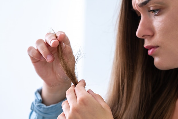 Porträt der unglücklichen traurigen Frau des Umkippens mit der schädigenden Haarlocke, die unter trockenem Haar und aufgeteilten Enden leidet.