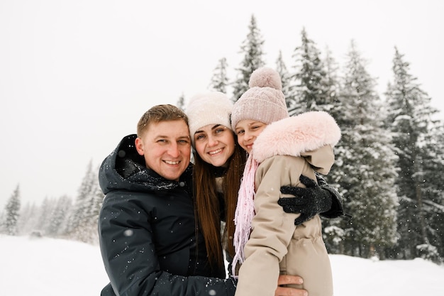 Porträt der verspielten glücklichen Familie im Winterwald. Mutter, Vater und Tochter spielen mit Schnee. Genießen Sie die gemeinsame Zeit. Familienkonzept