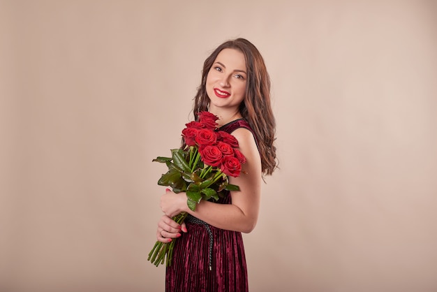 Porträt der zufriedenen jungen Frau im roten Kleid mit Rosenstrauß