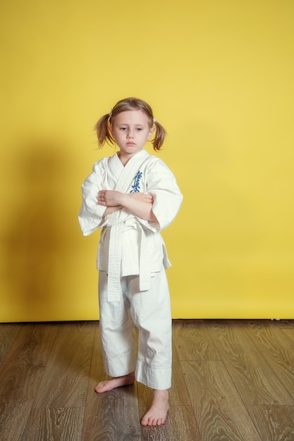 Porträt des 5 Jahre alten kaukasischen Mädchens im Kimono, das Karate gegen gelben Hintergrund zu Hause praktiziert
