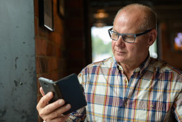 Porträt des älteren Geschäftsmannes, der Telefon am Kaffeehaus benutzt