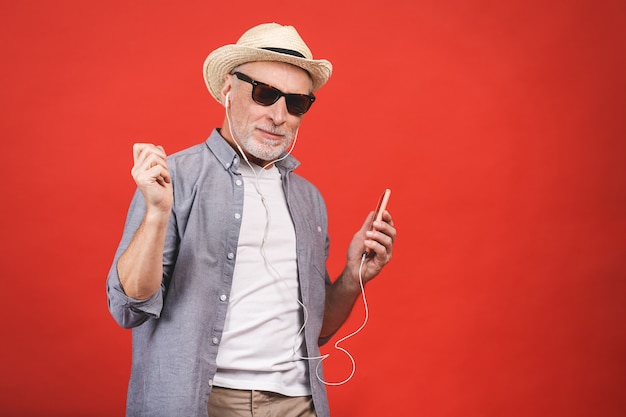 Porträt des älteren glücklichen fröhlichen älteren Mannes tanzend und hörende Musik mit Telefon und Kopfhörern isoliert.