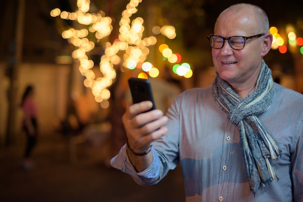 Porträt des älteren gutaussehenden skandinavischen Touristenmannes, der die Stadtstraßen in der Nacht erkundet