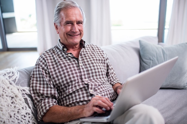 Porträt des älteren Mannes, der Laptop im Wohnzimmer verwendet