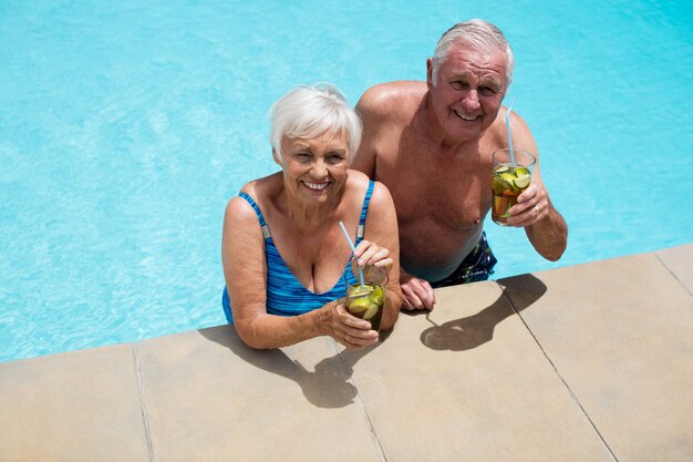 Porträt des älteren Paares, das Gläser Eistee im Pool hält