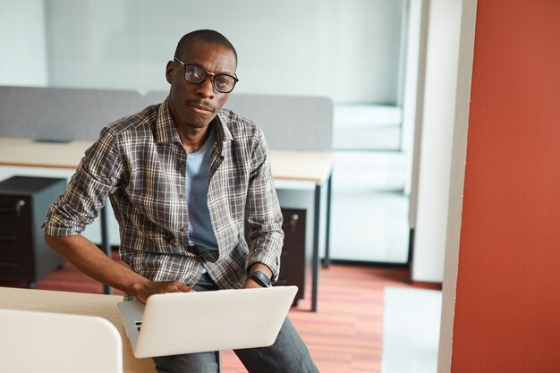 Porträt des afrikanischen Designers in der Brille, während er seinen Laptop bei der Arbeit benutzt