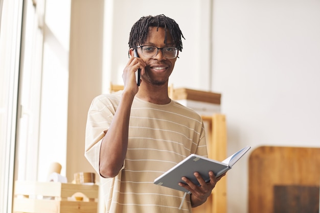 Porträt des afrikanischen jungen Mannes, der auf digitalem Tablett arbeitet und die Bestellung durch das Telefon nimmt