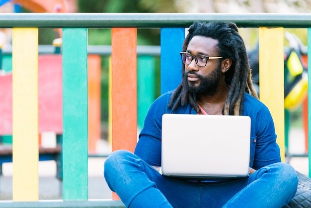 Porträt des afrikanischen Mannes, der draußen mit Laptop sitzt. Urbanes Arbeitskonzept