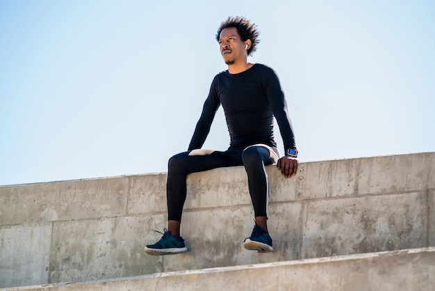 Porträt des Afro-Athletenmannes, der sich entspannt und nach der Arbeit im Freien sitzt