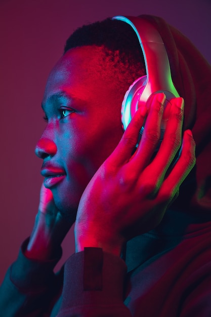 Porträt des afroamerikanischen Mannes mit Kopfhörern auf Gradientenstudiohintergrund im Neonlicht. Schönes männliches Model singen, tanzen. Konzept der menschlichen Emotionen, Gesichtsausdruck, Verkauf, Anzeige, Inklusion.