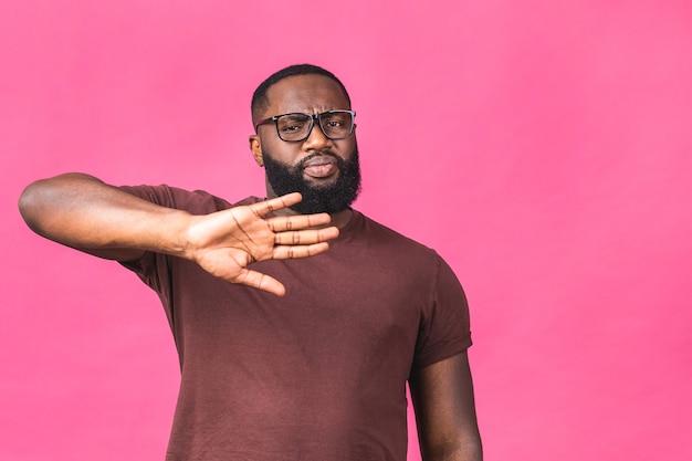 Porträt des afroamerikanischen schwarzen Mannes, der die Hand im Stoppschild hält, Sie warnt und vor etwas Schlechtem schützt und die Kamera mit besorgtem Ausdruck einzeln auf rosafarbenem Hintergrund anschaut.