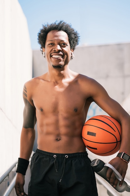 Porträt des Afroathletenmannes, der einen Basketballball hält und sich nach dem Training im Freien entspannt