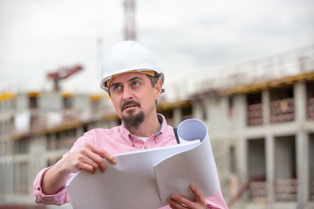 Porträt des Architekten bei der Arbeit mit Helm auf einer Baustelle, liest den Plan, Papierprojekte