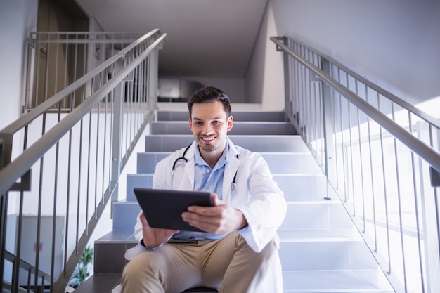 Porträt des Arztes, der auf Treppe mit digitalem Tablett sitzt