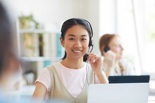 Porträt des asiatischen Betreibers im lächelnden Headset während der Arbeit im Callcenter