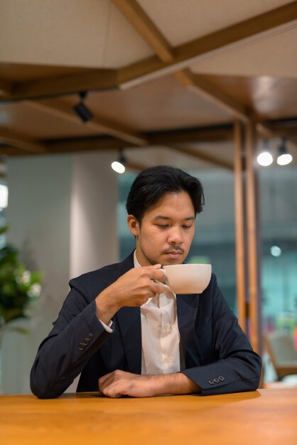 Porträt des asiatischen geschäftsmannes im kaffeehaus, das kaffee trinkt