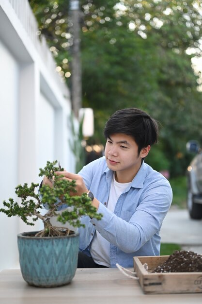 Porträt des asiatischen Mannes schneidet Bonsai-Pflanze mit Astschere in seinem Hausgarten.