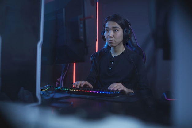 Porträt des asiatischen Teenagers unter Verwendung des Computers beim Spielen von Videospielen im dunklen Raum, Kopierraum