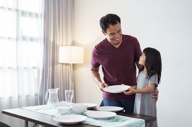 Porträt des asiatischen vaters und der kleinen tochter, die esstisch für abendessen vorbereiten