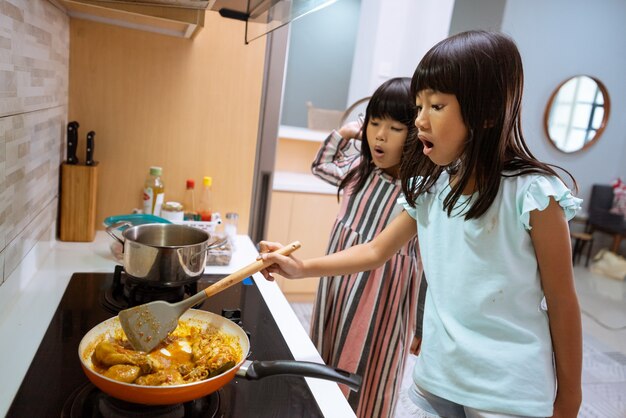 Porträt des asiatischen zwei kleinen Mädchens, das in der Küche kocht