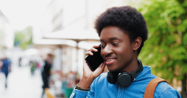 Porträt des attraktiven jungen Mannes, der draußen am Smartphone spricht, während er das Handy für...