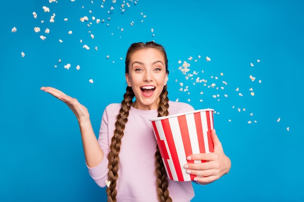 Porträt des aufgeregten enthusiastischen Mädchens halten Kasten mit fliegendem Popcorn, das in den wehenden Luftwind fällt, während Sie den Fernsehsender der Serie schreien sehen, wow omg tragen rosa Pullover isoliert über Glanzfarbe Hintergrund