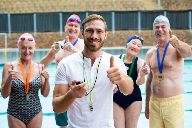 Porträt des Ausbilders und der älteren Schwimmer, die Daumen am Pool zeigen