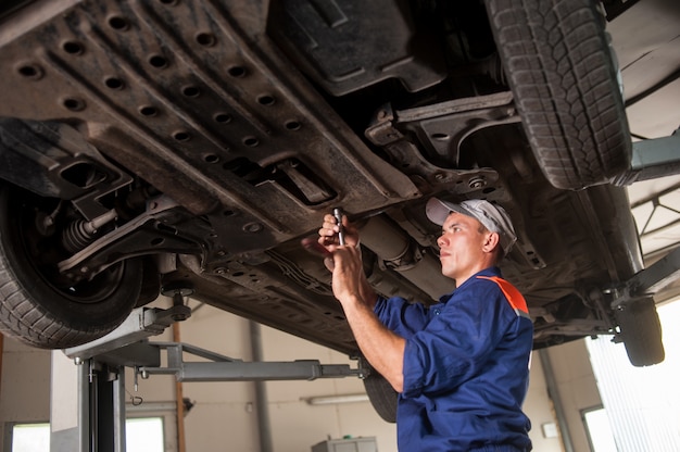 Porträt des Automechanikers arbeitend mit Werkzeugen unter Auto