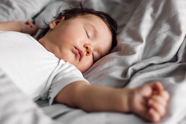 Porträt des Babys in Nachtwäsche, das zu Hause unter der Decke auf dem Bett liegt. Schlafendes Kleinkind im Schlafzimmer, siehe süßer Traum