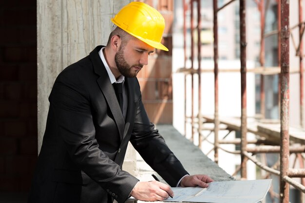 Porträt des Baumeisters mit gelbem Helm und Blaupause in den Händen