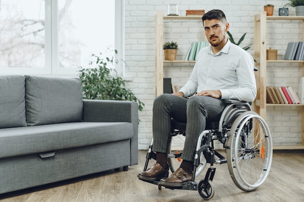 Porträt des behinderten Mannes in der formellen Kleidung, die in einem Rollstuhl drinnen sitzt