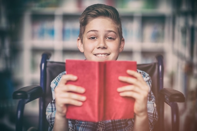 Porträt des behinderten Schülers, der Buch in der Bibliothek hält