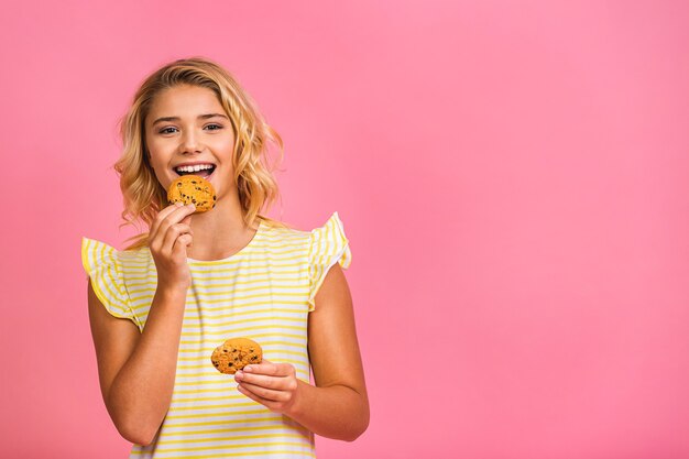 Porträt des blonden Teenager-Mädchens des positiven Kinderkindes, das Schokoladenkekssnack isst, trägt lässig