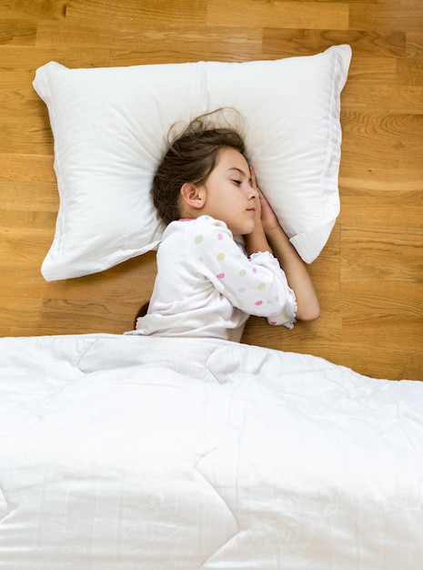 Porträt des brünetten kleinen Mädchens, das auf dem Boden mit Decke bedeckt schläft