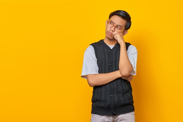 Porträt des denkenden asiatischen Mannes, der das Kinn berührt und den leeren Raum über gelbem Hintergrund betrachtet