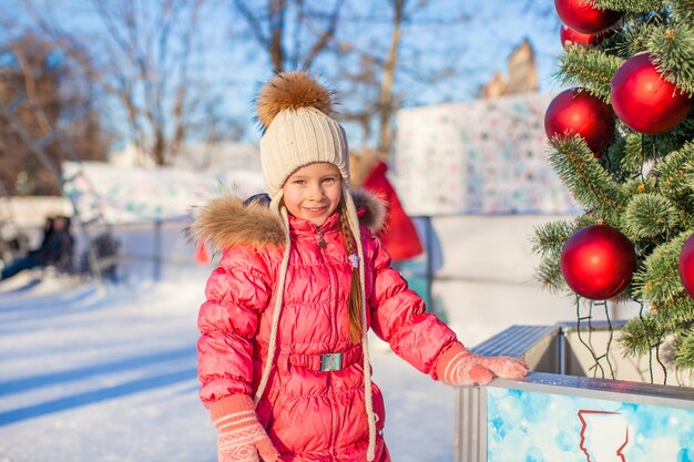 Porträt des entzückenden kleinen Mädchens nahe Weihnachtsbaum auf Eisbahn