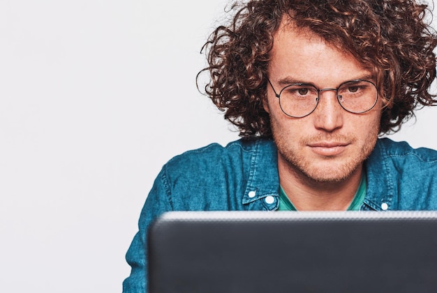 Foto porträt des ernsten jungen mannes, der an seinem schreibtisch mit laptop sitzt nahaufnahmebild des kaukasischen geschäftsmannes, der im büro arbeitet, das über weißer wand aufwirft