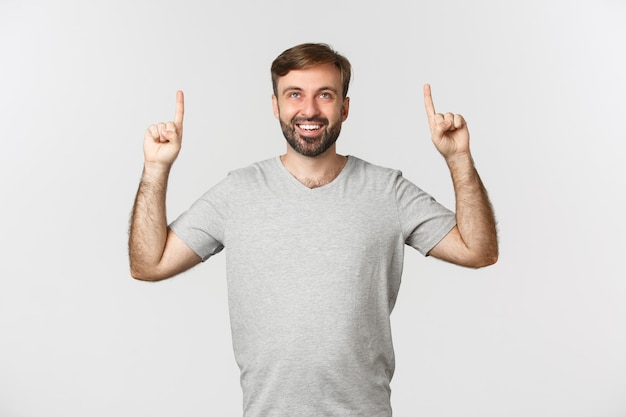 Porträt des erstaunten lächelnden Kerls mit einem Bart, der graues T-Shirt trägt