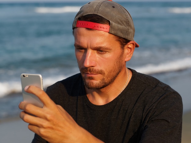 Porträt des gebräunten Mannes am Strand mit Handy. Lebensstile.