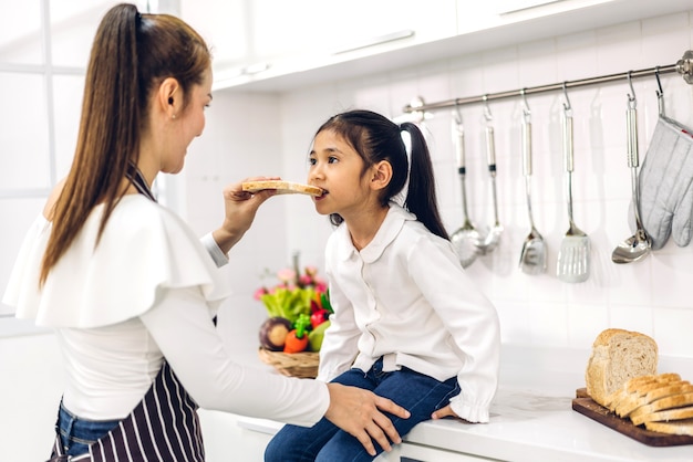 Porträt des Genießens der glücklichen Liebe asiatische Familienmutter und des kleinen asiatischen Mädchenkindes lächelnd und Vorbereitung des Kochens des Frühstücks zusammen in der Küche zu Hause