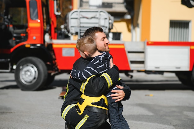 Porträt des geretteten kleinen Jungen mit Feuerwehrmann, der in der Nähe des Feuerwehrautos steht Feuerwehrmann im Brandbekämpfungseinsatz