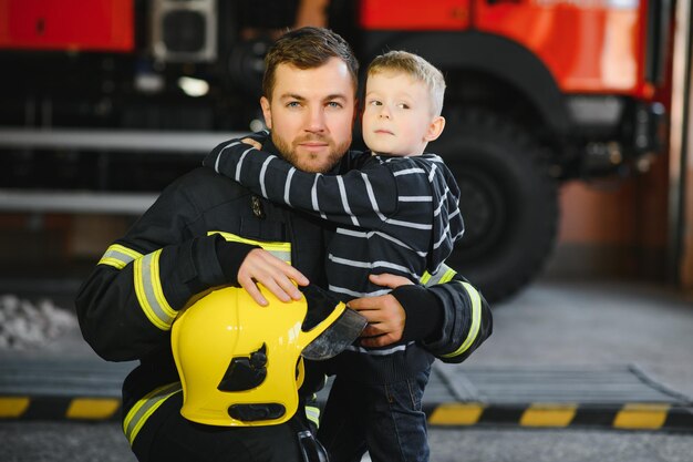 Porträt des geretteten kleinen jungen mit feuerwehrmann, der in der nähe des feuerwehrautos steht feuerwehrmann im brandbekämpfungseinsatz