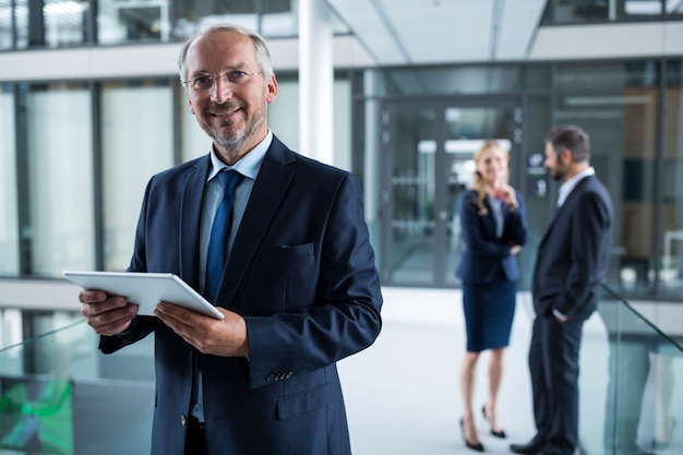 Porträt des Geschäftsmannes, der digitales Tablett und Kollegen hält, die im Hintergrund sprechen