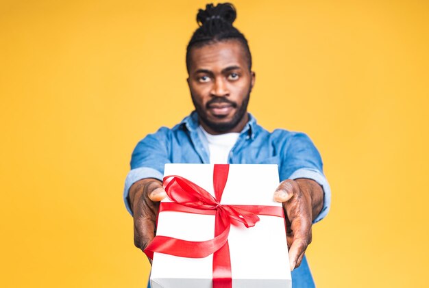 Porträt des glücklichen afroamerikanischen schwarzen Mannes, der Geschenkbox hält, lokalisiert über gelbem Studiohintergrund. Feiertage feiern.