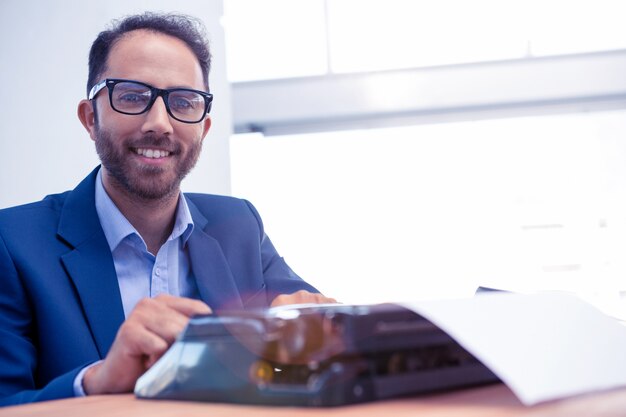 Porträt des glücklichen Geschäftsmannes arbeitend an Schreibmaschine beim Sitzen im hellen Büro