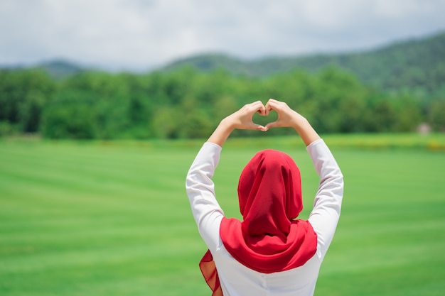 Porträt des glücklichen jungen moslemischen roten hijab am grünen Feld