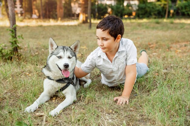 Porträt des glücklichen kaukasischen Jungen mit seinem Hund, der auf Rasen liegt