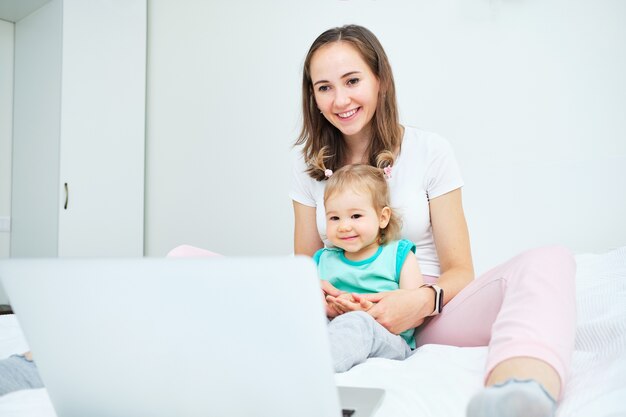 Porträt des glücklichen kaukasischen Kindes und der Mutter, die auf Sofa sitzen und Video auf Laptop ansehen